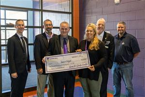 Jamie Wyse holding a novelty check & SHEF Board smiling for the Teacher Excellence Grant presentation at TSES